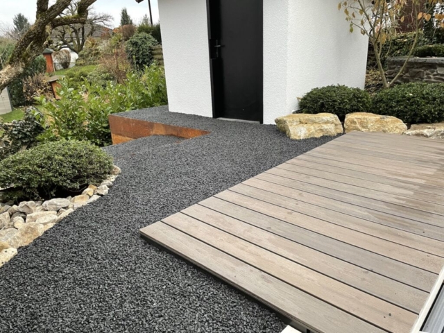 Weg aus Basalt um eine Holzterrasse.