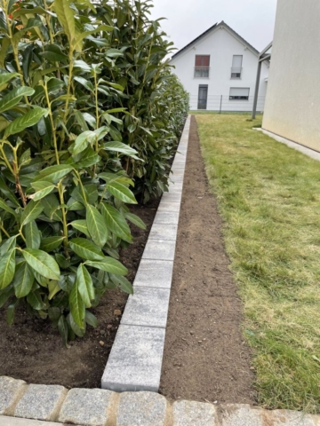 Der Weg zum Garten am Haus vorbei ist links mit einer Hecke bepflanzt und einem Einzeiler vom Rasen getrennt.